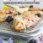 A hand drizzles icing on a berry scone placed on a cooling rack, with blackberries, lemon slices, and purple flowers around. Text reads: "18 Scone Recipes with Big Flavor in Every Bite.