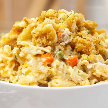 A white bowl filled with creamy pasta mixed with vegetables and topped with pieces of breaded, crispy chicken—an easy dinner perfect for weeknight recipes.