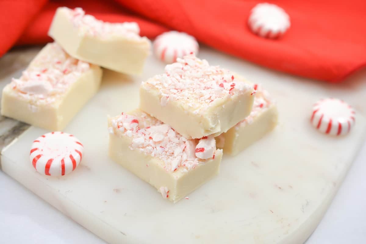 Three pieces of white chocolate peppermint bark topped with crushed peppermint candy are stacked on a white marble surface, perfect for adding festive flair to your holiday table and ideal for those seeking vegetarian Christmas recipes.