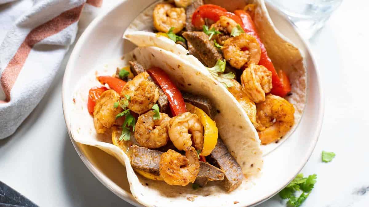 Two flour tortillas filled with shrimp, beef strips, red and yellow bell peppers, and garnished with cilantro, served on a white plate&mdash;a perfect one-and-done meal for busy weeknights.