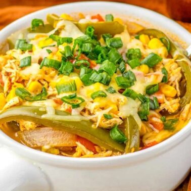 A bowl of chicken fajita soup topped with melted cheese and chopped green onions sits on the table, served with a spoon and crunchy tortilla chips for a bold flavor experience.