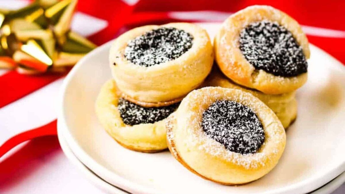 A white plate with a stack of round cookies filled with chocolate and dusted with powdered sugar, set against a festive background with red ribbon and a gold bow&mdash;perfect for those who love European-Inspired Recipes.
