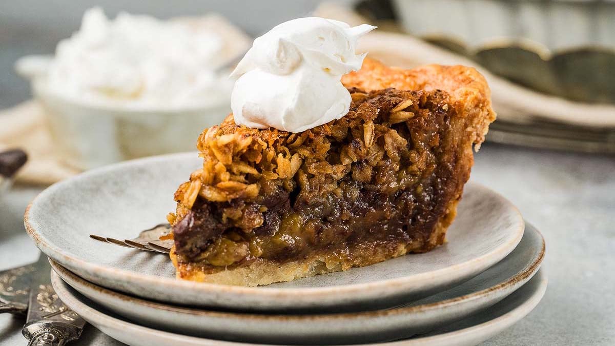 A slice of oatmeal pie topped with a dollop of whipped cream sits on a stack of gray plates with a fork beside it—one of those easy Thanksgiving desserts that looks truly impressive.