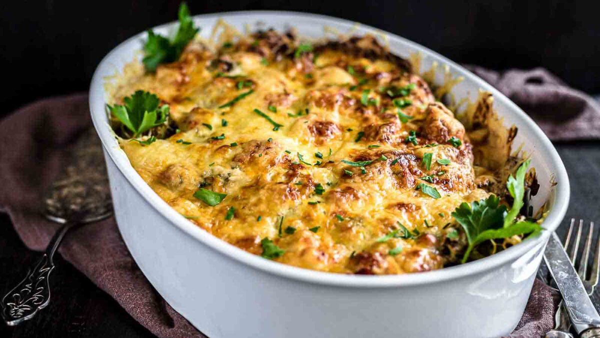 A baked casserole in a white oval dish topped with melted, browned cheese to satisfy your cravings and garnished with fresh parsley—a must-try for fans of cheesy recipes.
