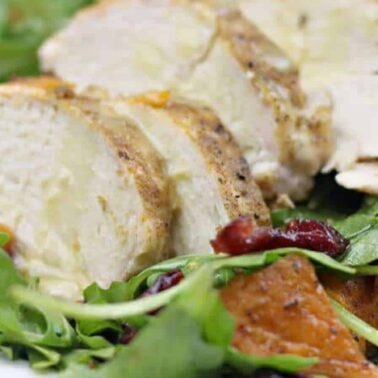 Sliced cooked chicken breast served on a bed of mixed greens with roasted sweet potatoes and dried cranberriesโone of our flavorful recipes perfect for easy cooking.