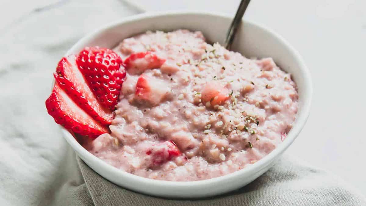 A white bowl of strawberry oatmeal, topped with sliced strawberries and sprinkled with seeds, sits invitingly with a spoon—perfect inspiration for your next oatmeal recipes.
