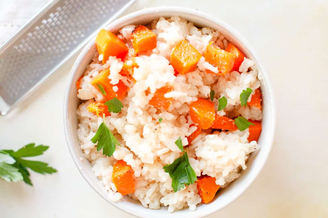 A bowl of cooked white rice mixed with diced carrots and tender butternut squash, garnished with fresh parsley—a simple addition for those seeking flavorful recipes.