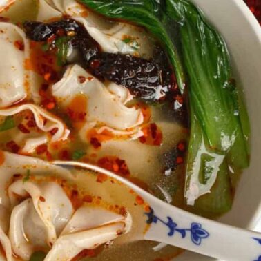 A bowl of hearty soup with wide noodles, leafy greens, and chili oil, served with a ceramic spoon; seaweed and extra chili oil are in small dishes on the side—perfect for comforting winter soups.