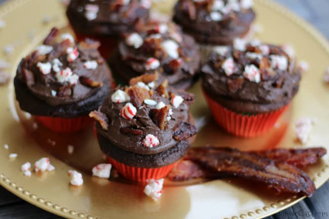 Chocolate cupcakes with chocolate frosting, topped with crumbled bacon and crushed peppermint, arranged on a gold plate with bacon strips—a bold twist on holiday recipes and a fun spin on peppermint desserts.