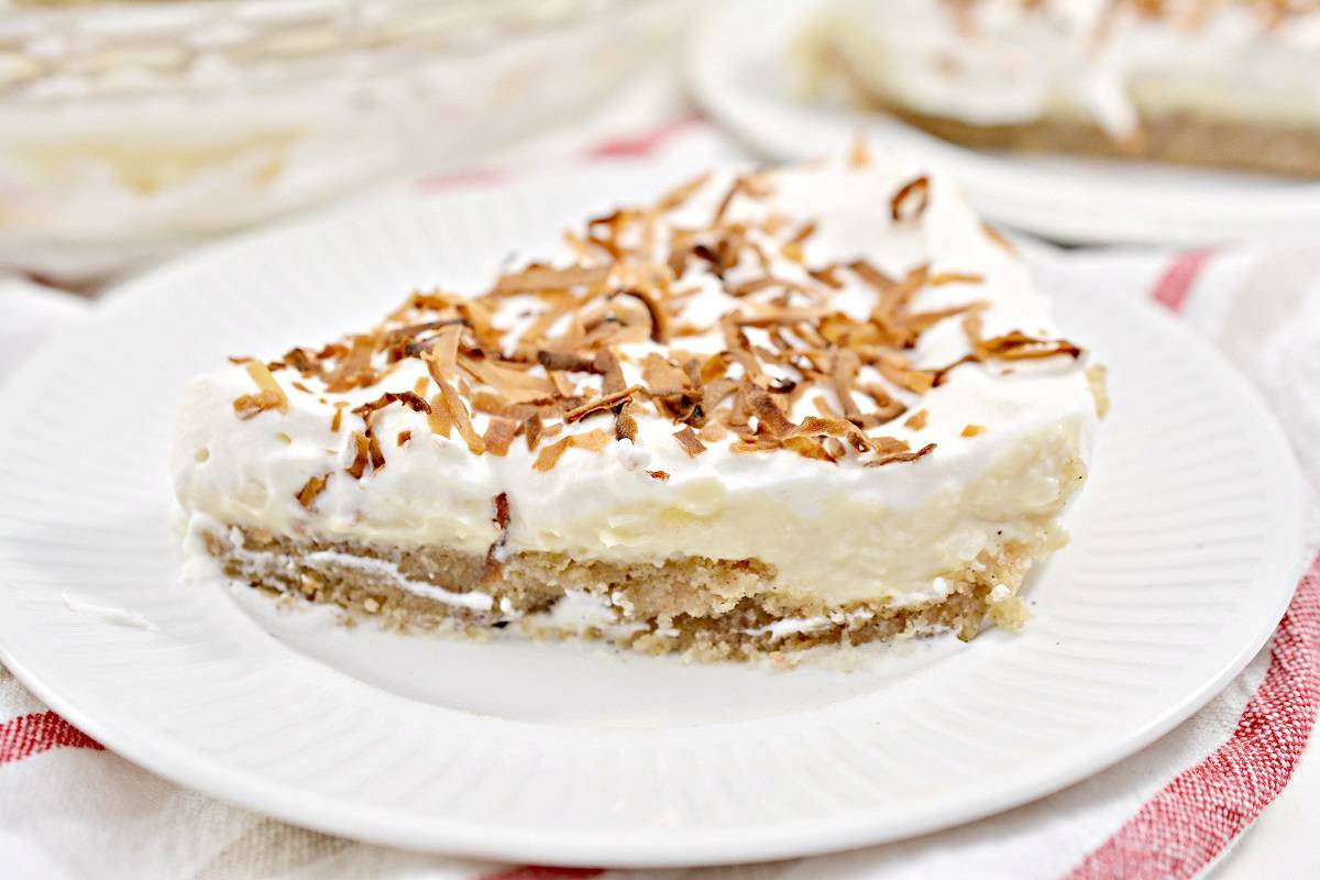 A slice of cream pie topped with toasted coconut flakes on a white plate&mdash;perfect for anyone who loves bold baking and irresistible desserts.