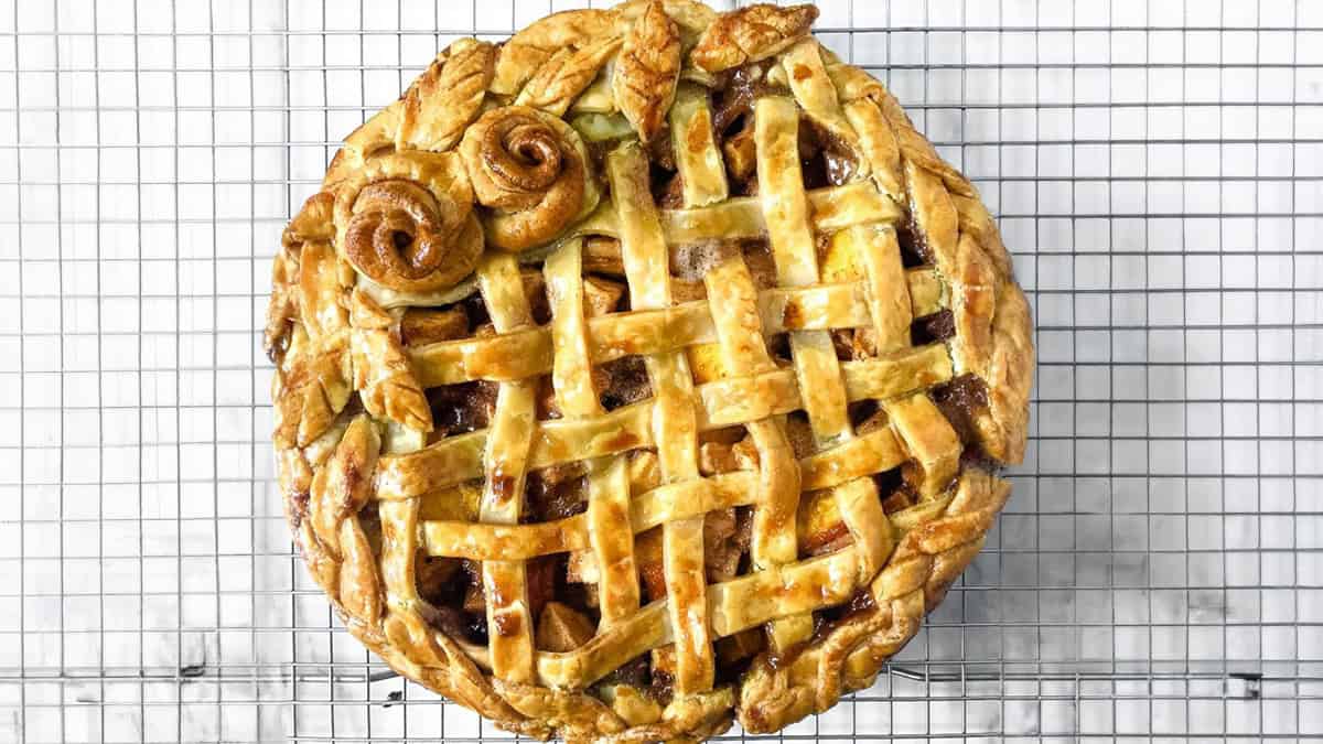 A baked lattice-top pie with decorative pastry roses on one side, resting on a wire cooling rack, offers wholesome flavor and a delightful crunch from crunchy walnuts.
