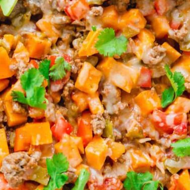 Close-up of a colorful ground beef skillet with diced sweet potatoes, tomatoes, melted cheese, bell peppers, and fresh cilantro, garnished with lime wedges—a year-round favorite for fans of sweet potato recipes.