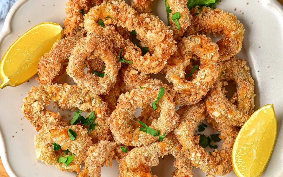 A plate of breaded and baked calamari rings garnished with chopped parsley, served with lemon wedges&mdash;enjoy this air fryer appetizer for crisp flavor without the oil.