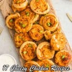 A wooden board with swirled cheesy chicken pinwheels garnished with chopped green onions, alongside a fork and plates. Text reads: "17 Cheesy Chicken Recipes That Fit Every Meal and Mood.