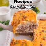 A cheesy casserole slice being served from a baking dish, with text overlay: "18 Cozy Casserole Recipes for Cold Nights.