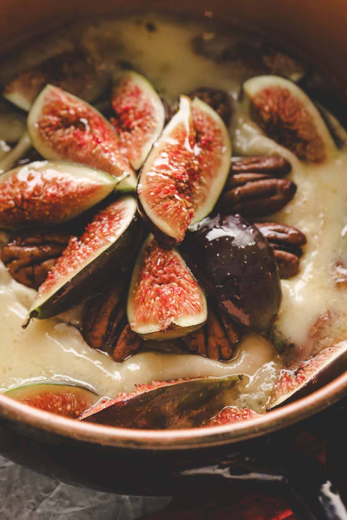 Sliced figs and pecans arranged in a creamy melted cheese inside a brown ceramic dish.