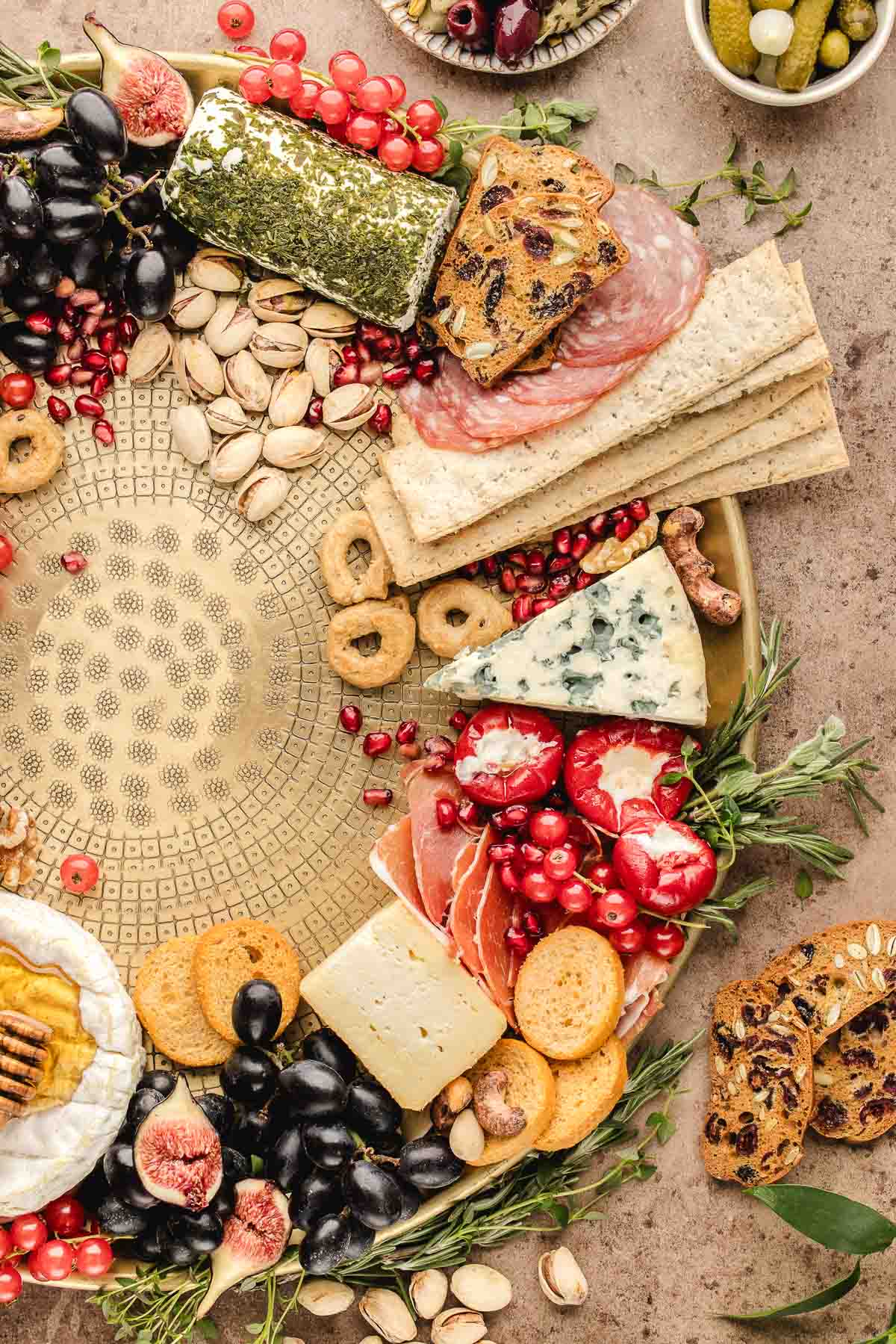 A charcuterie board with assorted cheeses, meats, crackers, fresh fruits, nuts, bread, and olives arranged around a decorative round platter.