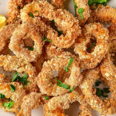 A plate of breaded and baked calamari rings garnished with chopped parsley, served with lemon wedges on the sideโperfect as air fryer appetizers for your next party.