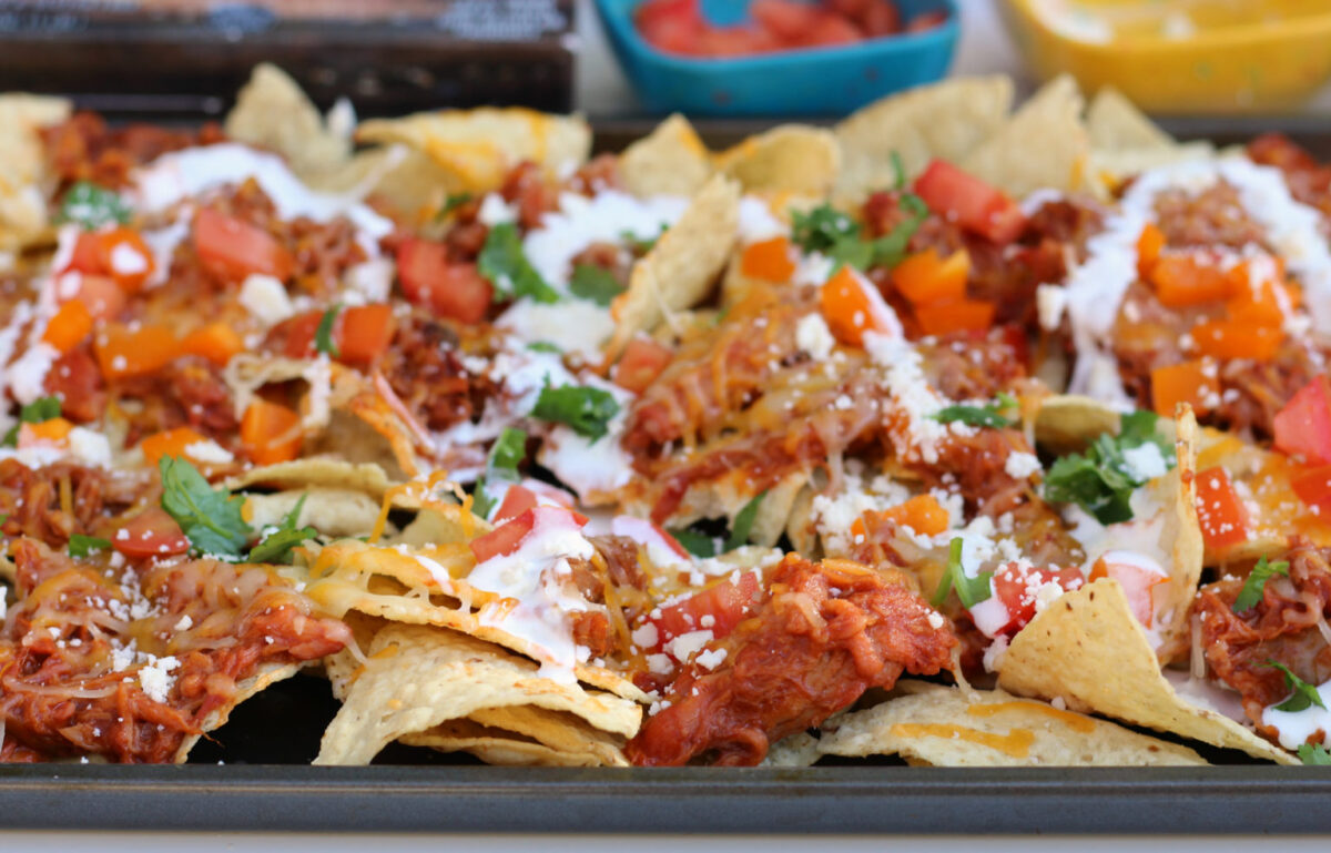 A tray of nachos topped with shredded meat, melted cheese, chopped tomatoes, cilantro, and drizzled with sour cream brings backyard energy to your table&mdash;perfect for fans of classic BBQ recipes.