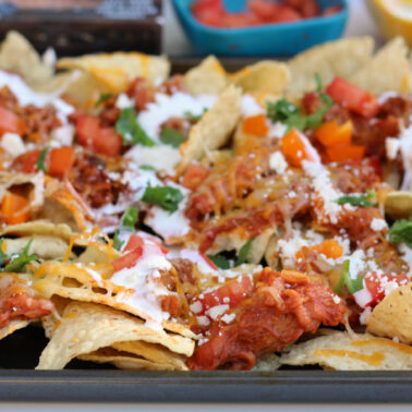 A tray of nachos topped with shredded meat, melted cheese, chopped tomatoes, cilantro, and drizzled with sour cream brings backyard energy to your tableโperfect for fans of classic BBQ recipes.