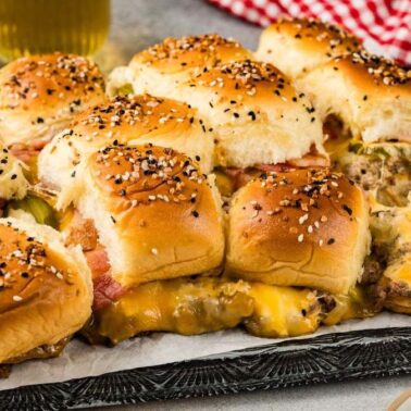 A tray of cheeseburger sliders with sesame seed buns, melted cheese, pickles, and beef patties served on parchment paperโperfect savory appetizers for any gathering.