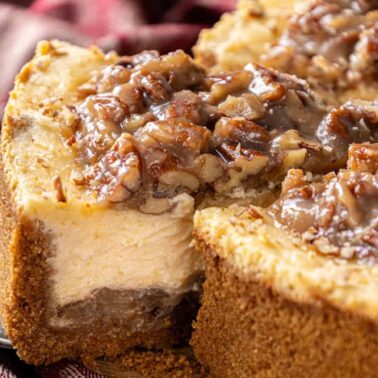 A close-up of a sliced cheesecake with a crumb crust, topped with chopped pecans and a glossy caramel-like sauceโa true comfort recipe perfect for those who cherish nostalgic meals.