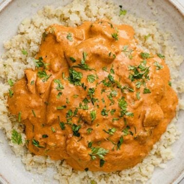 A plate of cauliflower rice topped with a creamy, orange-colored sauce that delivers a rich butter flavor, and garnished with chopped herbs—a delightful addition to your collection of savory recipes.