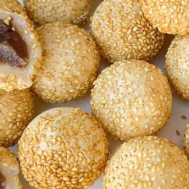 A plate of golden sesame balls, some with a bite taken out to reveal a dark sweet filling inside—these make for delightful egg-free recipes bursting with rich flavor.