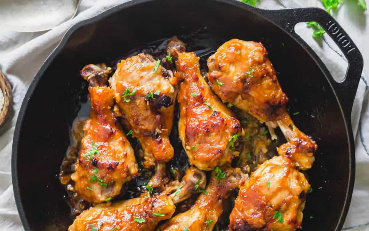 Cooked chicken drumsticks with a glazed, browned surface are arranged in a black cast iron skillet and garnished with chopped herbs for an umami-rich, Asian-style dinner.
