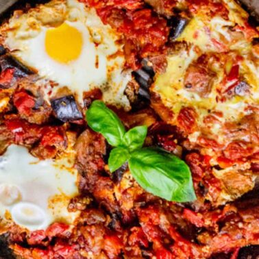 A skillet filled with shakshuka: poached eggs in a tomato and vegetable sauce, garnished with a sprig of fresh basil—perfect for hearty vegetarian breakfast ideas.