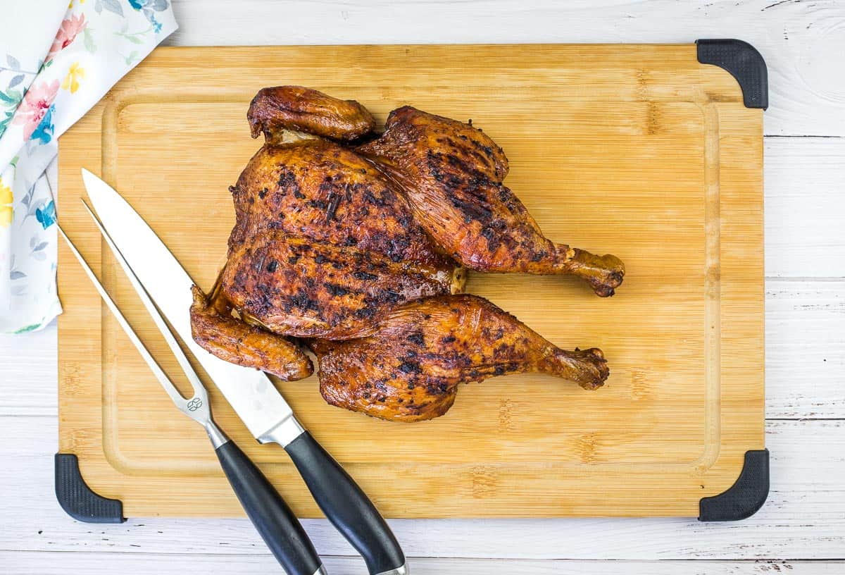 A cooked, spatchcocked chicken on a wooden cutting board with a chef’s knife and carving knife beside it—perfect inspiration for fire-kissed flavor and new grilled chicken recipes.