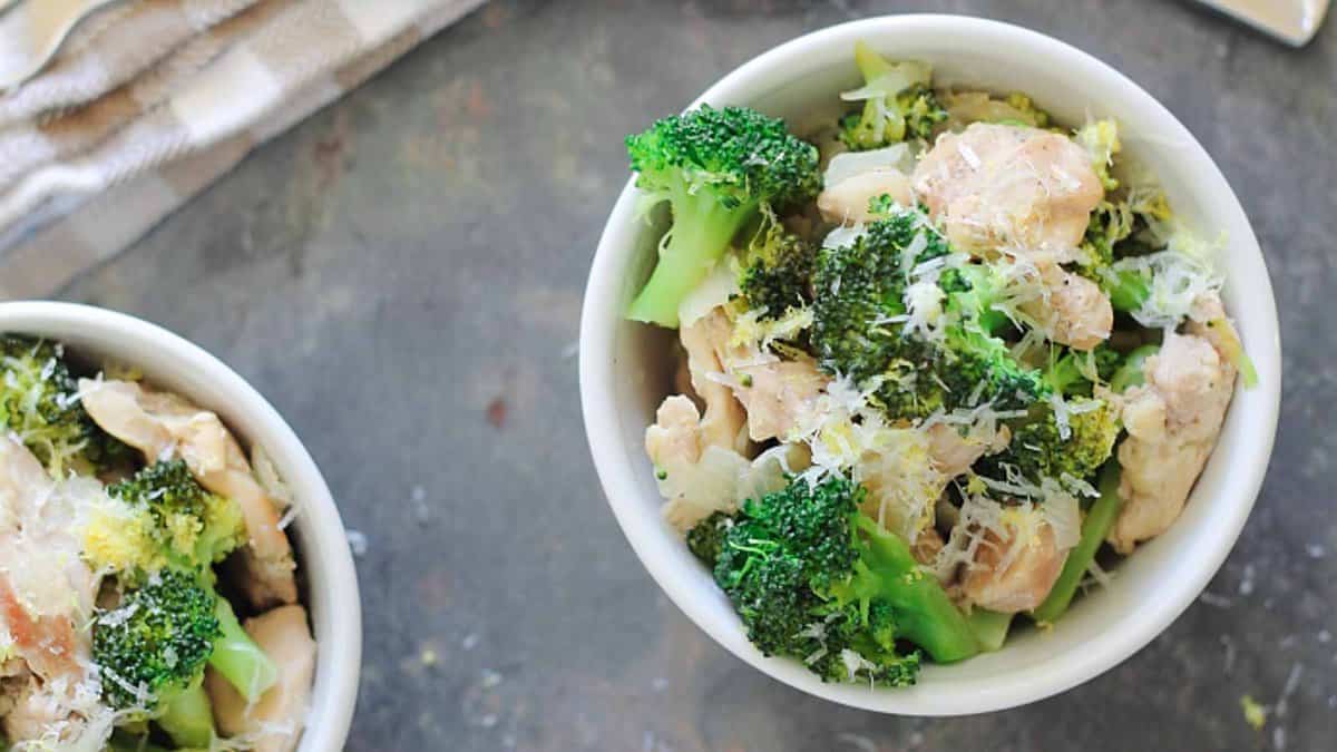 A white bowl filled with cooked broccoli, chicken pieces, and grated cheese&mdash;perfect for everyday meals or special meals&mdash;sits on a gray surface.