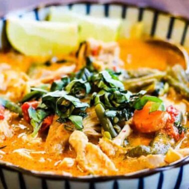 A bowl of Thai red curry with vegetables, chicken, and fresh herbs delivers cozy spice, served with lime wedges and a spoon.