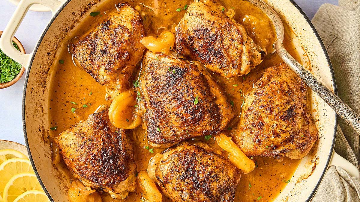 Six browned chicken thighs in a pan with a golden, seasoned sauce and apricot pieces, garnished with herbs—a flavorful dinner perfect for those seeking delicious gluten-free recipes.