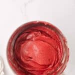 A mixing bowl filled with smooth, red cake batter sits on a white marble countertop.