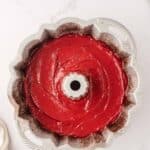 A Bundt pan filled with smooth red cake batter on a white marble surface.