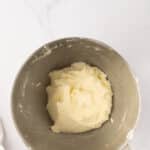 A stainless steel mixing bowl with a pale, creamy dough mixture inside, placed on a white marble surface.