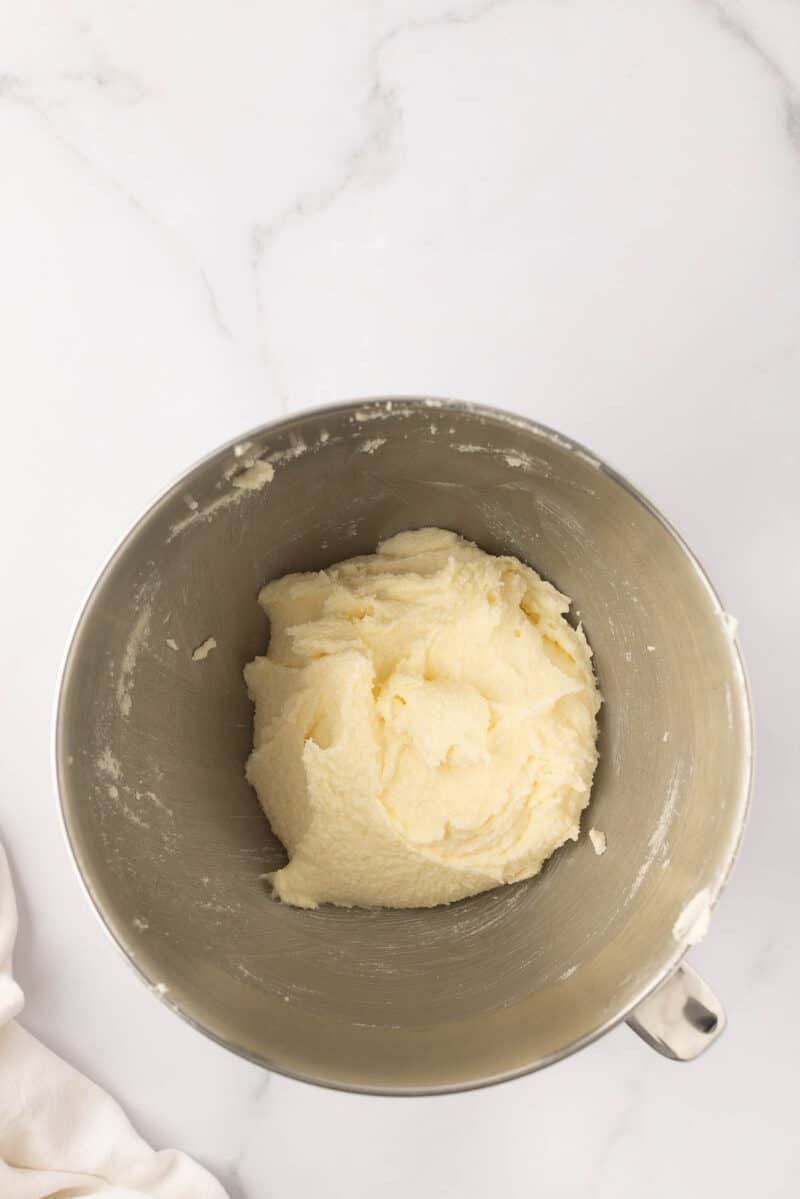 A stainless steel mixing bowl with a pale, creamy dough mixture inside, placed on a white marble surface.