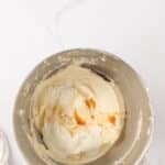 A metal mixing bowl containing a creamy batter with liquid ingredients, likely vanilla and milk, on a white marble surface.