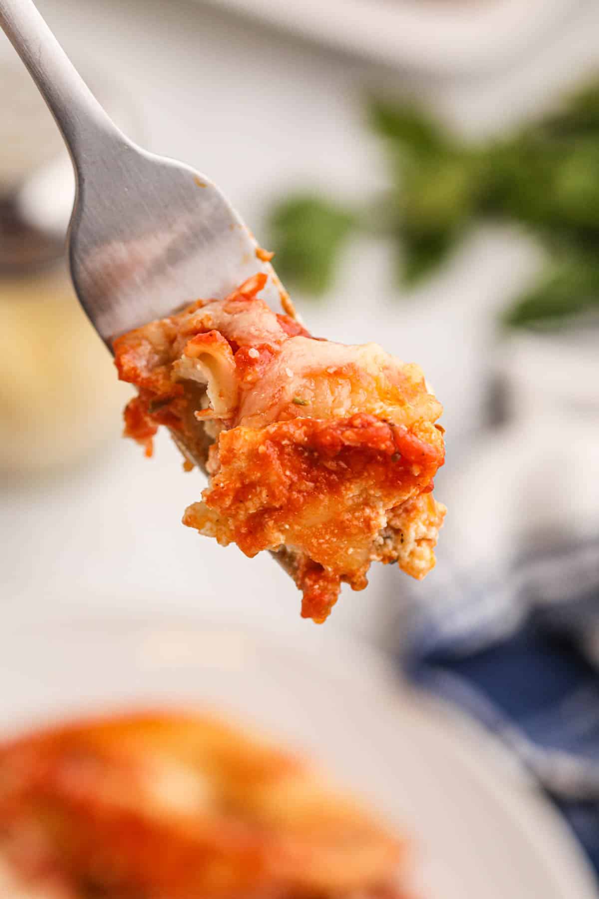 A fork holds a bite of cheesy, saucy lasagna above a blurred plate and background.