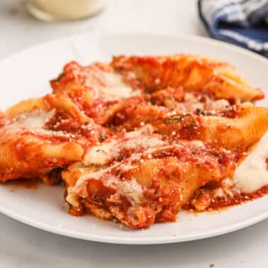 A white plate with stuffed pasta shells topped with tomato sauce and melted cheese, garnished with a sprinkle of herbs.