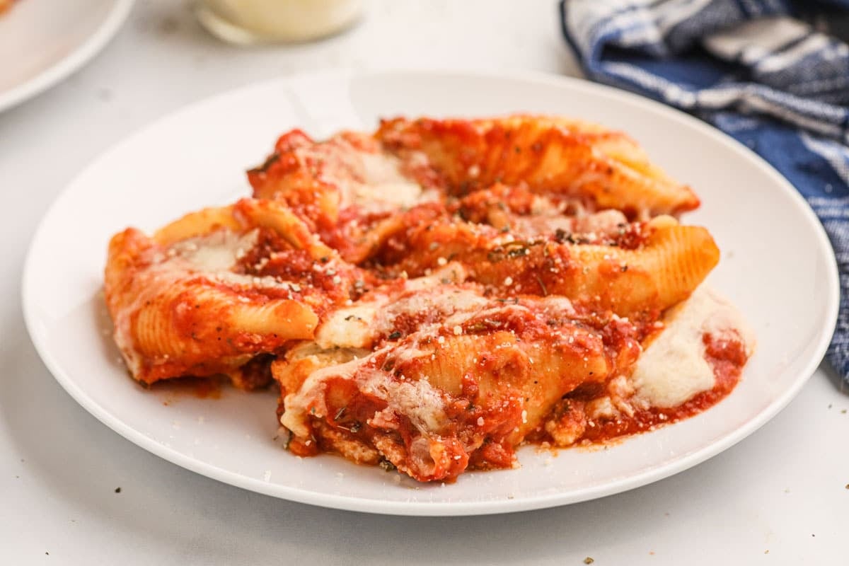 A white plate with stuffed pasta shells topped with tomato sauce and melted cheese, garnished with a sprinkle of herbs.