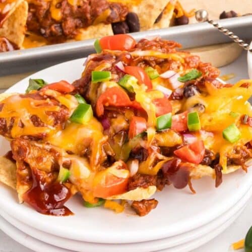 A plate of nachos topped with melted cheese, chopped tomatoes, onions, jalapeños, black beans, and barbecue sauce.