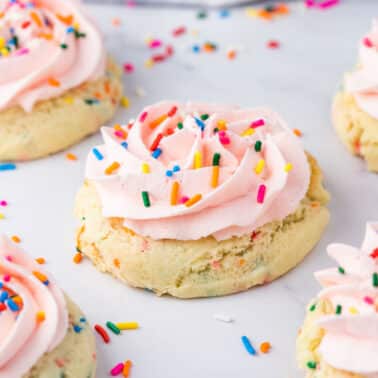 Five birthday cake cookies with pink icing and colorful sprinkles on a white surface.