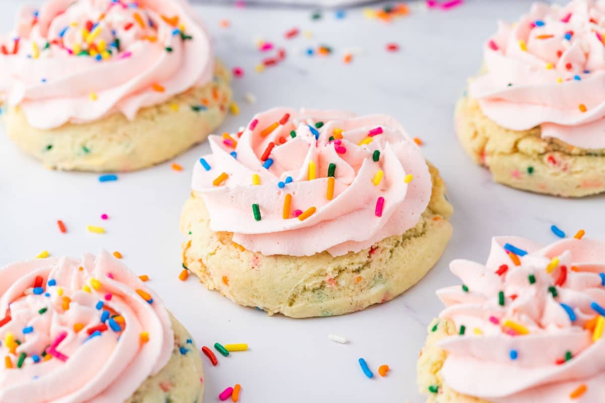 Five birthday cake cookies with pink icing and colorful sprinkles on a white surface.
