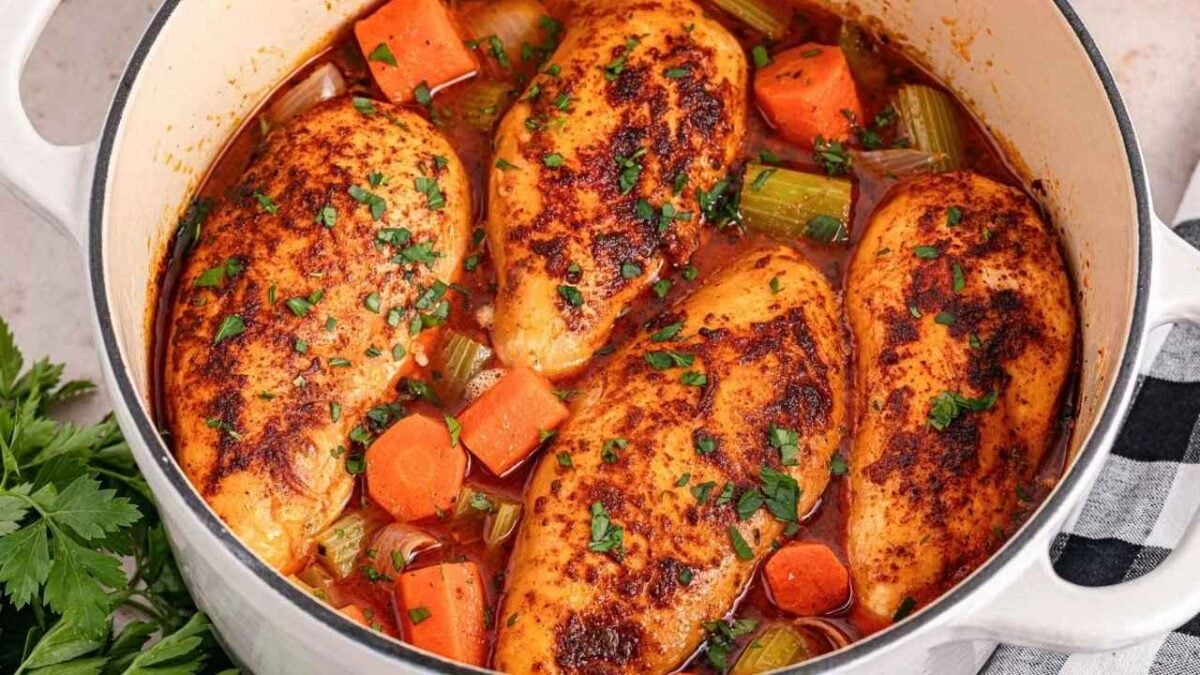 Four juicy chicken breasts simmer in a Dutch oven with carrots, celery, and sauce, topped with parsley—an easy prep favorite for delicious chicken breast recipes.