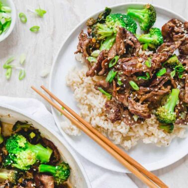 A plate of beef and broccoli stir-fry served over white rice, garnished with sliced green onionsโa perfect choice for fans of fast beef recipesโwith chopsticks placed on the side.