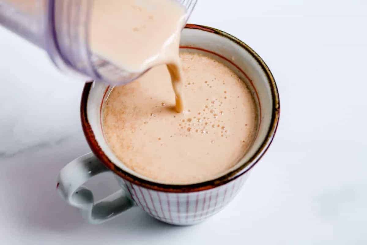 Creamy liquid being poured from a blender into a white mug with red stripes, perfect for creating special coffee drinks or trying new coffee recipes on a crisp white surface.