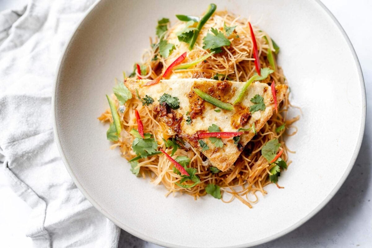 A plate of stir-fried vermicelli noodles topped with two pieces of omelette, garnished with cilantro and sliced green and red peppers, brings bold flavor and inspiration for plant-based cooking.
