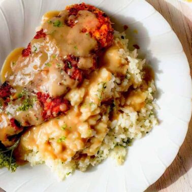 A plate of breaded chicken cutlets topped with savory gravy, served over rice and garnished with parsley.